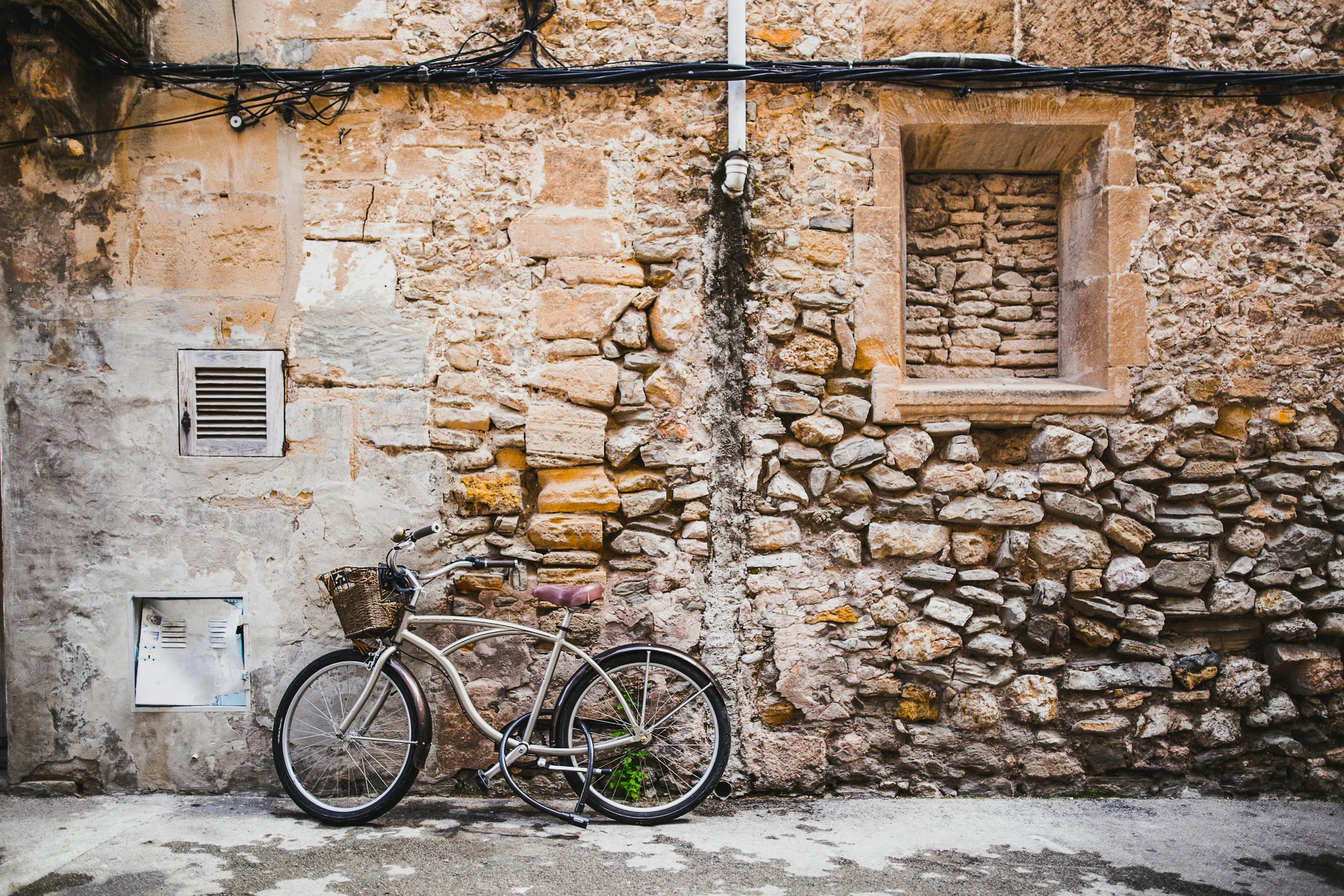 A city bicycle with a front basket and rear rack parked against a stone wall.